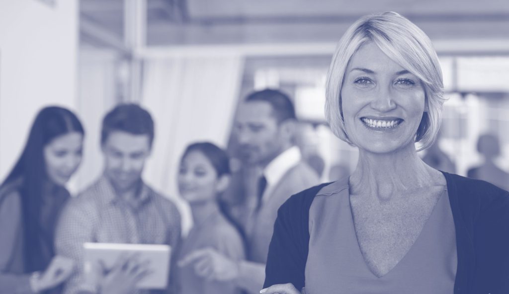 Emotionally Effective Workplaces A grey/blue lens with a lady smiling with people behind her. Teammates.