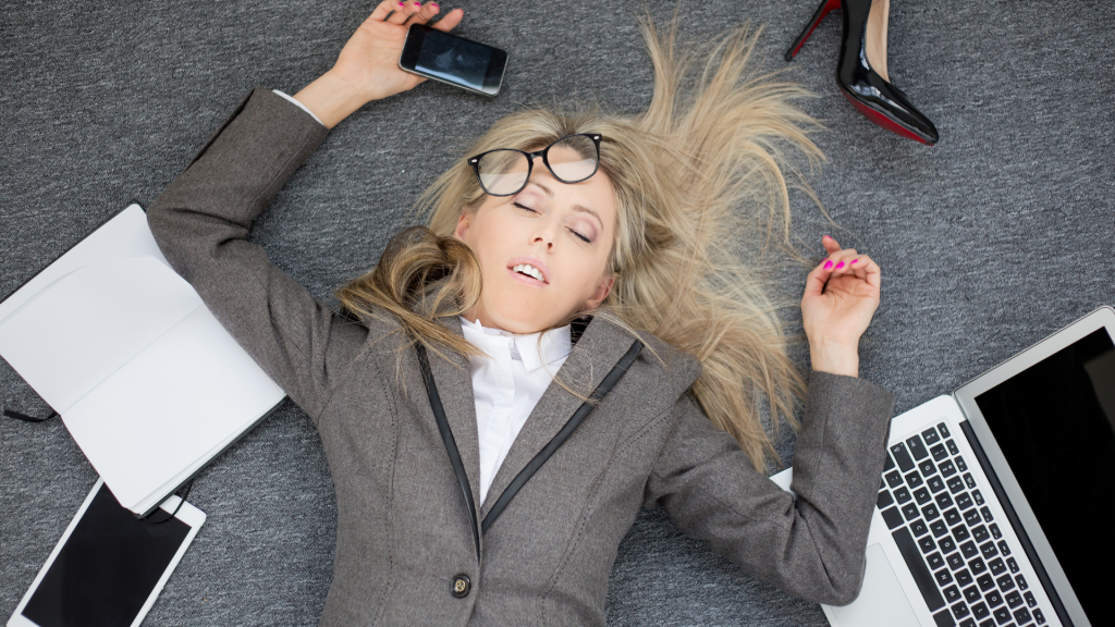 Imposter Syndrome This is a photo of a woman lying on the floor with her glasses hanging off, and devices strewn around. This image signifies burnout which is a characteristic of imposer syndrome.