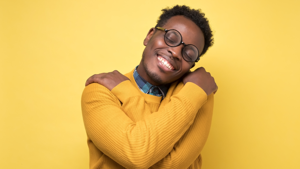 This is an image on a yellow background of a man hugging himself. This is to depict self-regard.